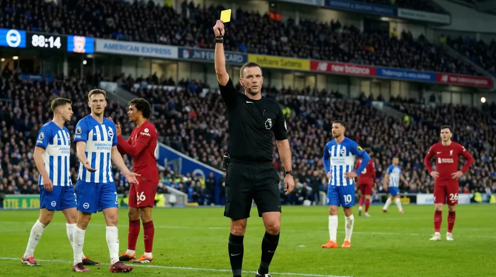 Árbitro de fútbol mostrando una tarjeta amarilla durante un partido profesional de la Ligue 1