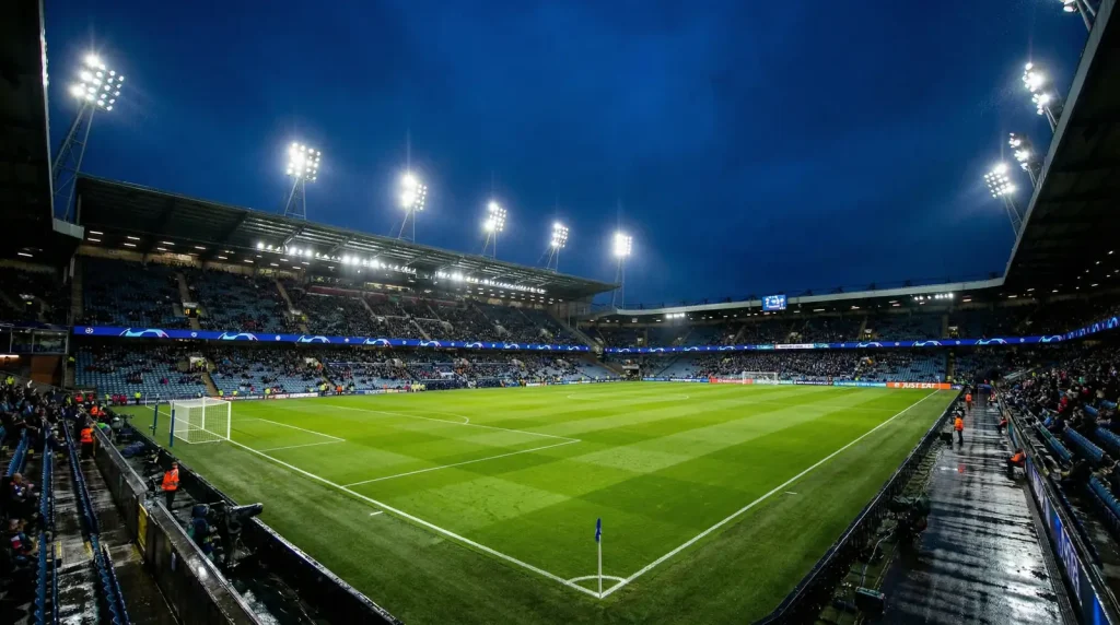 Estadio de fútbol europeo iluminado de noche con el césped perfectamente preparado para un partido de Champions